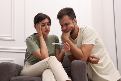 Photo of Worried young couple with pregnancy test at home