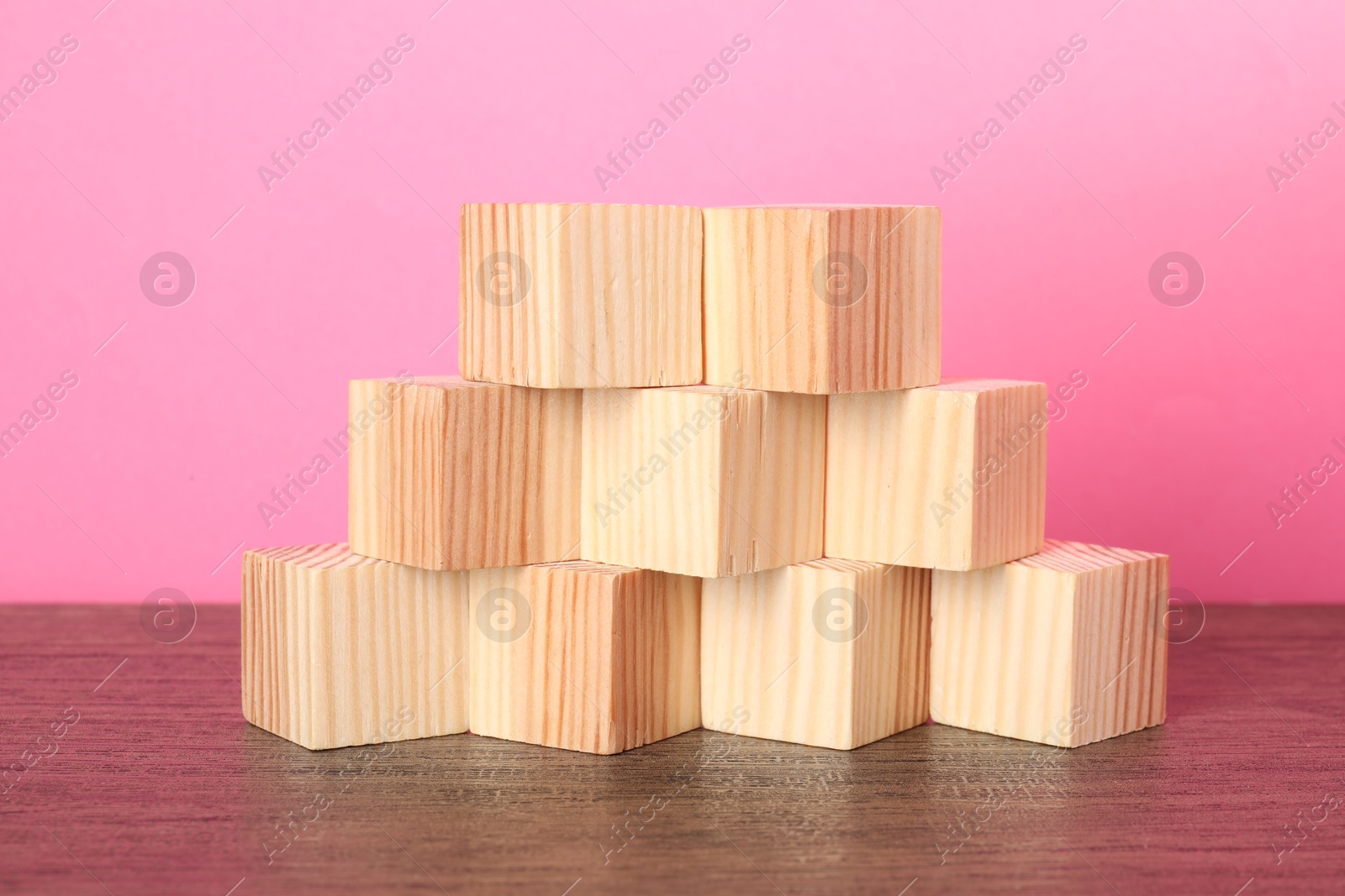 Photo of Many wooden cubes on table against pink background