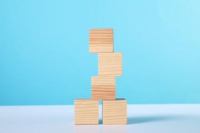 Photo of Stack of wooden cubes on white table against light blue background