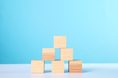 Photo of Many wooden cubes on white table against light blue background