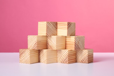 Photo of Many wooden cubes on white table against pink background