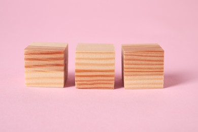 Three wooden cubes on pink background, closeup