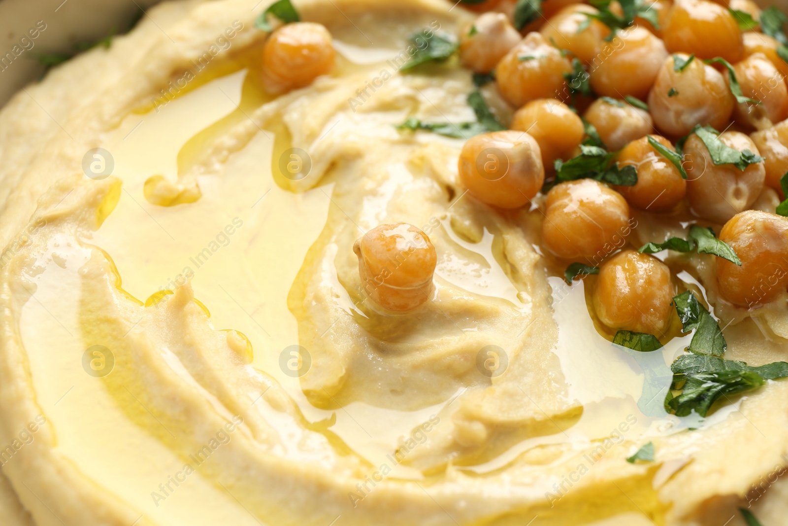 Photo of Delicious hummus with olive oil, chickpeas and parsley, closeup