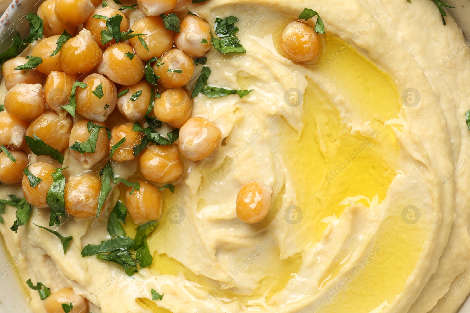 Photo of Delicious hummus with olive oil, chickpeas and parsley in bowl, top view