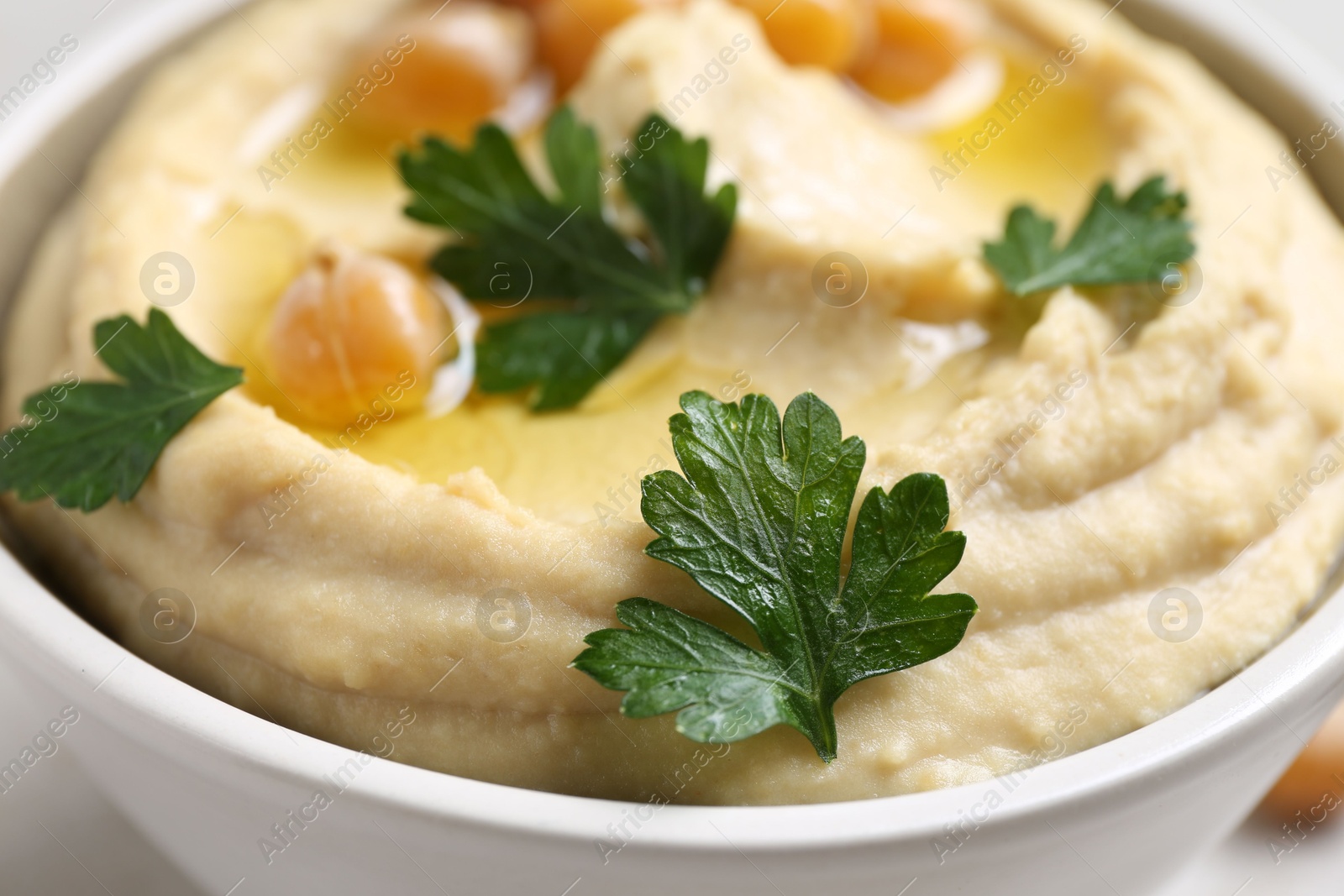 Photo of Delicious hummus with olive oil, chickpeas and parsley in bowl on table, closeup