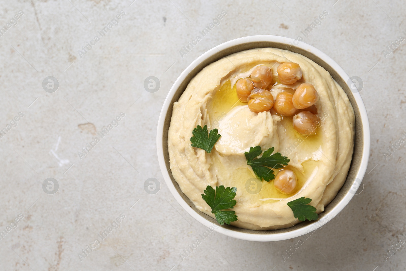 Photo of Delicious hummus with olive oil, chickpeas and parsley in bowl on light textured table, top view. Space for text