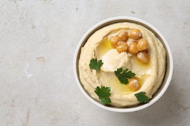 Photo of Delicious hummus with olive oil, chickpeas and parsley in bowl on light textured table, top view. Space for text