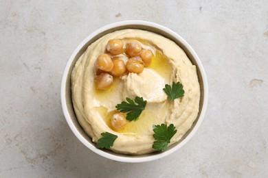 Delicious hummus with olive oil, chickpeas and parsley in bowl on light textured table, top view