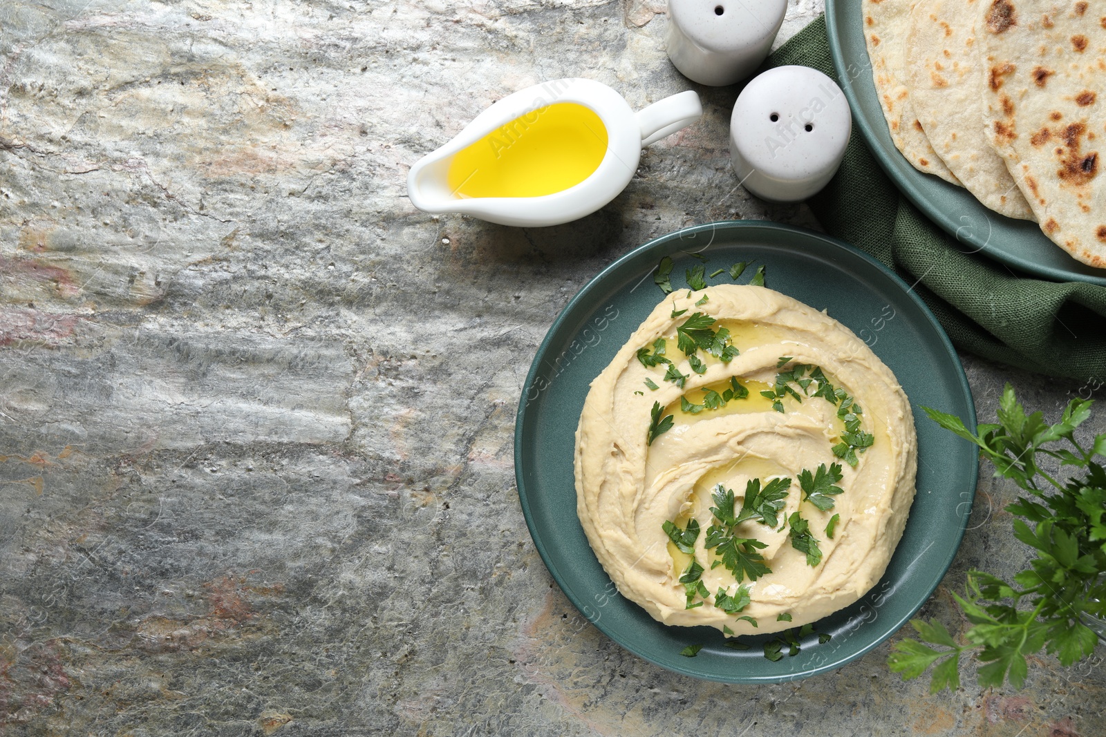 Photo of Delicious hummus with olive oil, pita and parsley on grey textured table, flat lay. Space for text