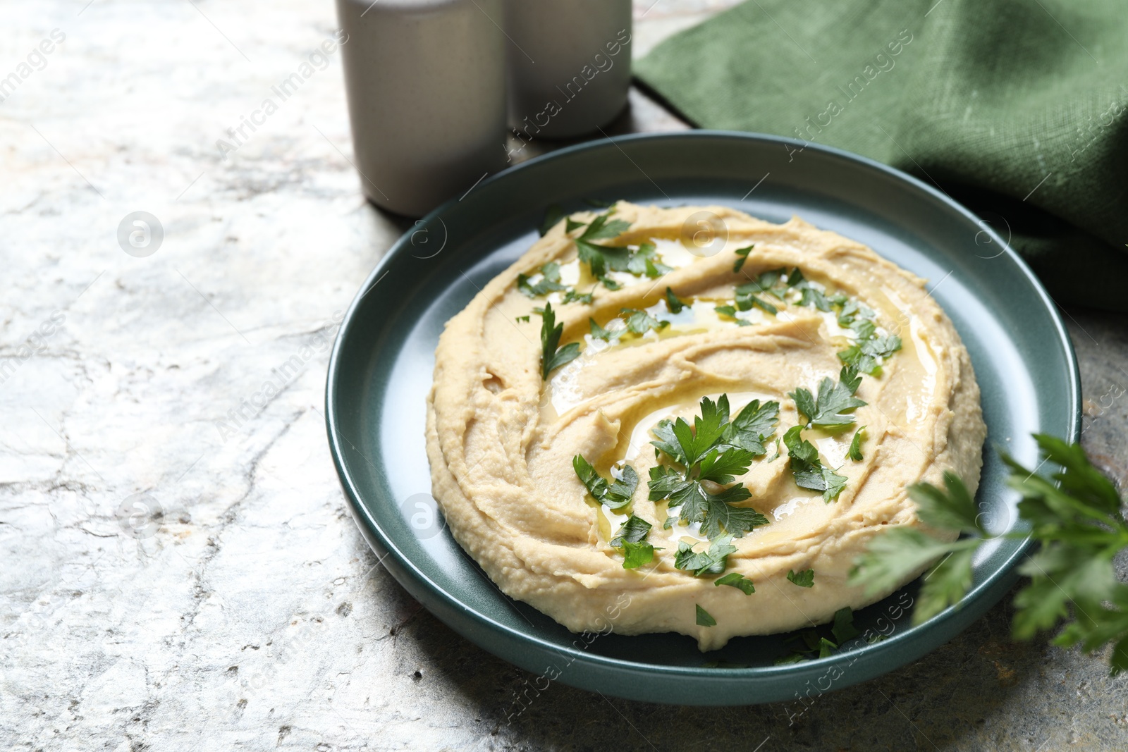 Photo of Delicious hummus with olive oil and parsley on grey textured table