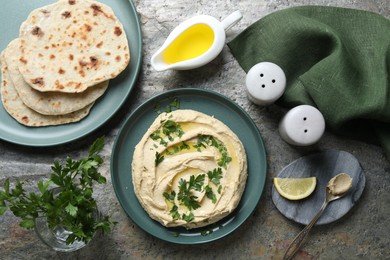 Photo of Delicious hummus with olive oil served on grey textured table, flat lay