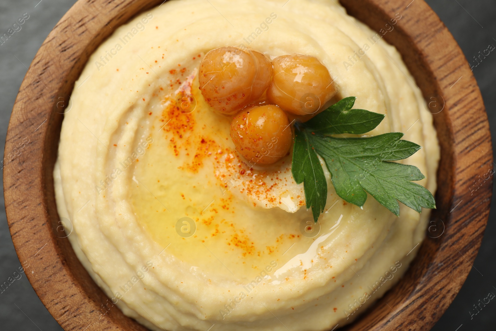 Photo of Delicious hummus with olive oil, chickpeas and parsley in bowl on grey table, top view