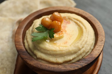 Photo of Delicious hummus with olive oil, chickpeas and parsley in bowl on grey table, closeup