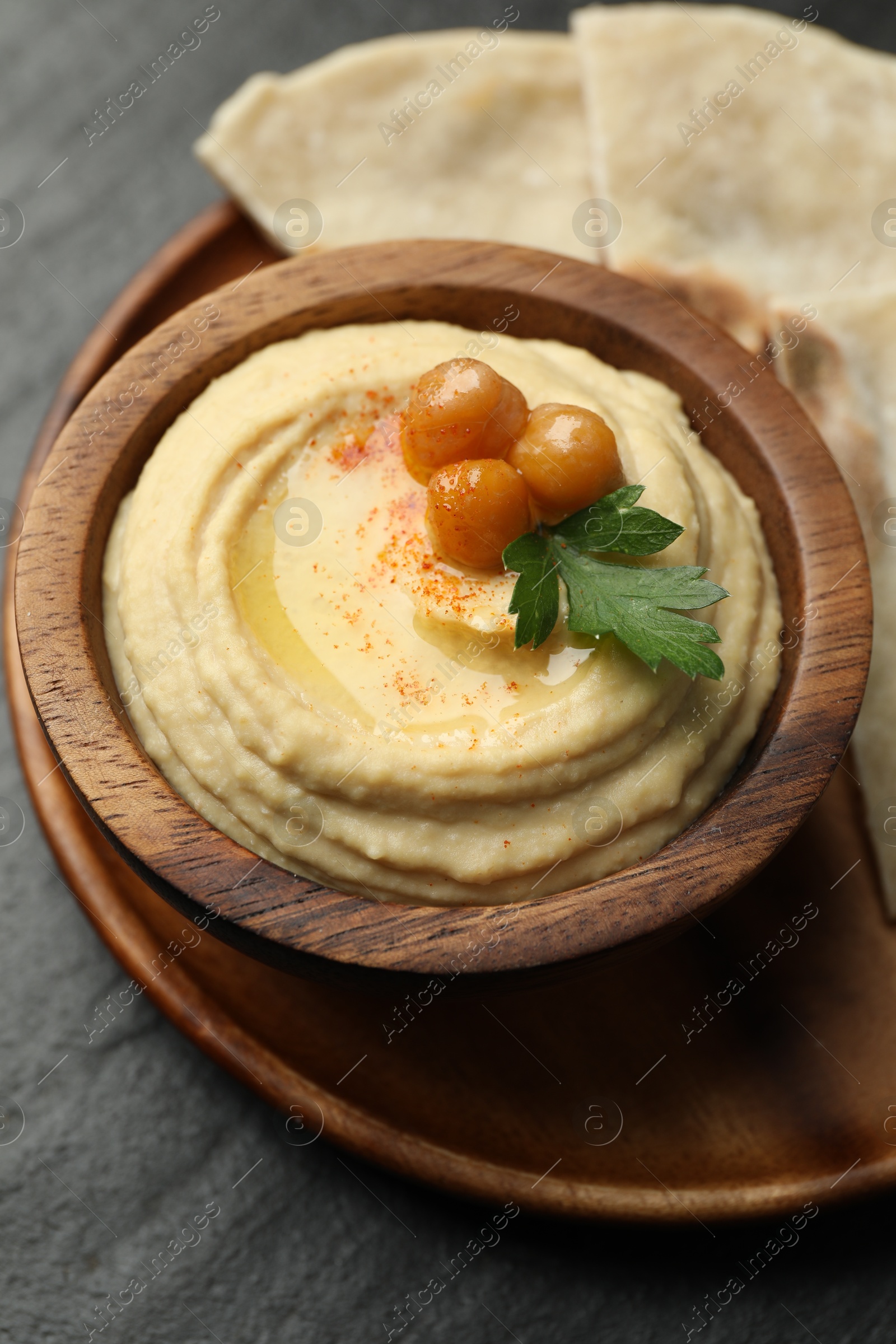 Photo of Delicious hummus with olive oil, chickpeas and parsley in bowl on grey table, closeup