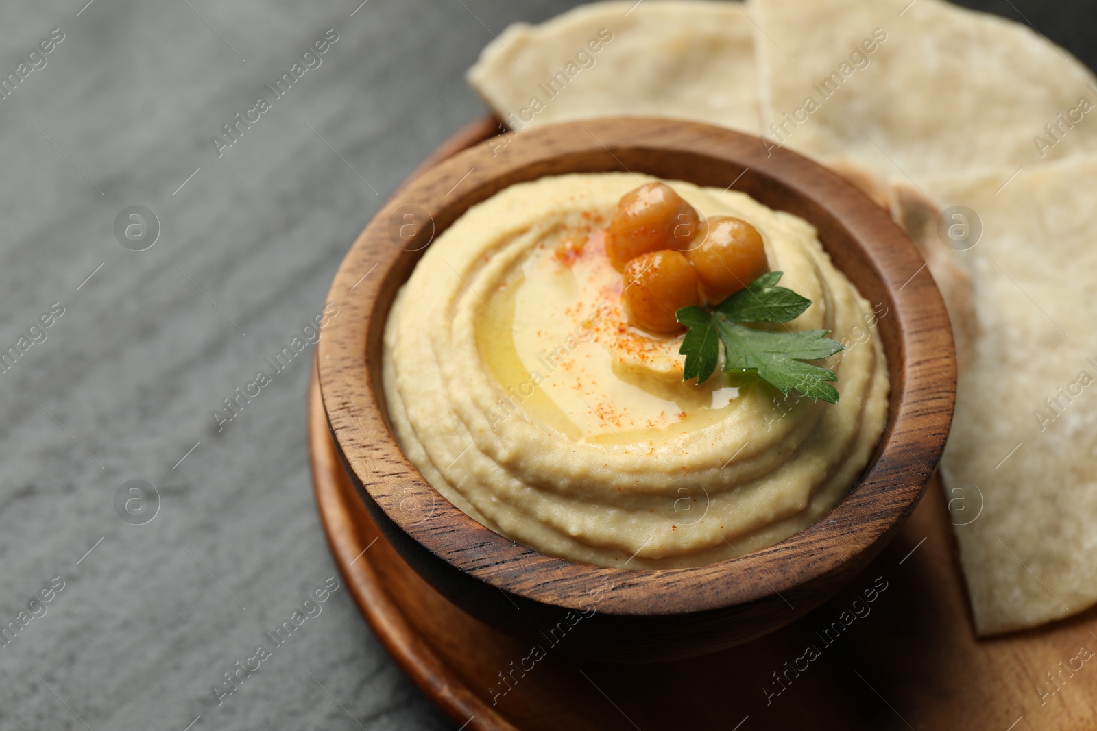 Photo of Delicious hummus with olive oil, chickpeas in bowl and pita on grey table, closeup