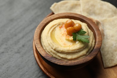 Photo of Delicious hummus with olive oil, chickpeas in bowl and pita on grey table, closeup