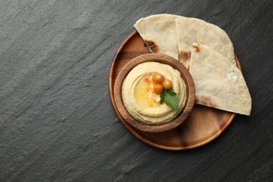 Photo of Delicious hummus with olive oil, chickpeas in bowl and pita on grey textured table, flat lay. Space for text