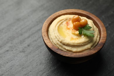 Photo of Delicious hummus with olive oil, chickpeas and parsley in bowl on grey textured table. Space for text