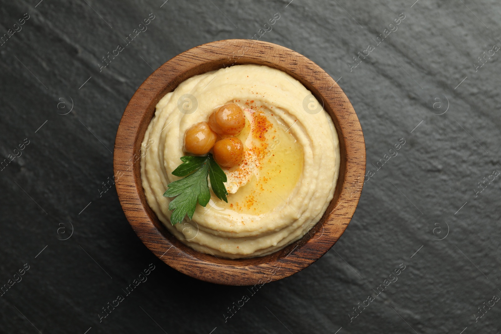 Photo of Delicious hummus with olive oil, chickpeas and parsley in bowl on grey textured table, top view