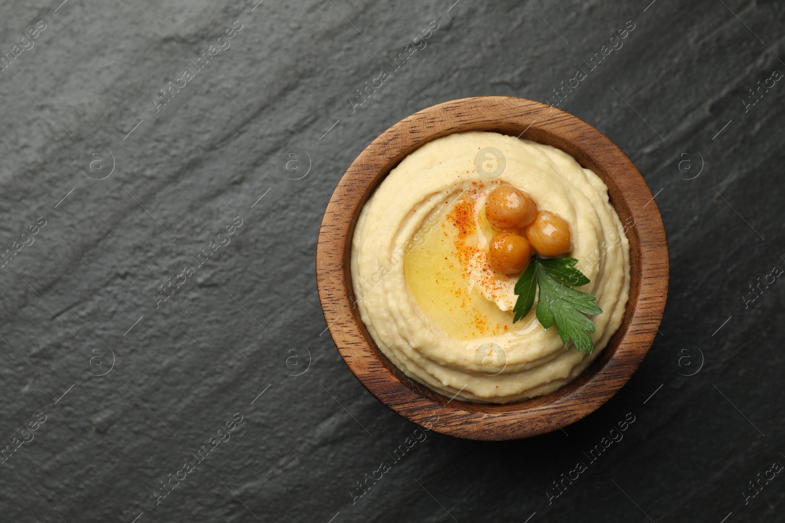 Photo of Delicious hummus with olive oil, chickpeas and parsley in bowl on grey textured table, top view. Space for text