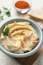 Photo of Delicious hummus with olive oil, parsley and paprika in bowl on white table, closeup