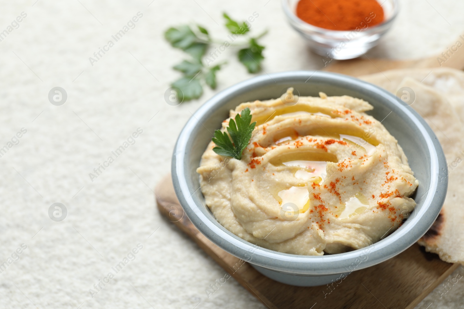 Photo of Delicious hummus with olive oil, parsley and paprika in bowl on white table, closeup. Space for text