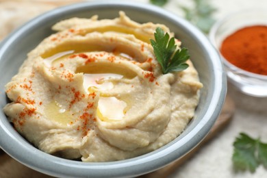 Delicious hummus with olive oil, parsley and paprika in bowl on white table, closeup