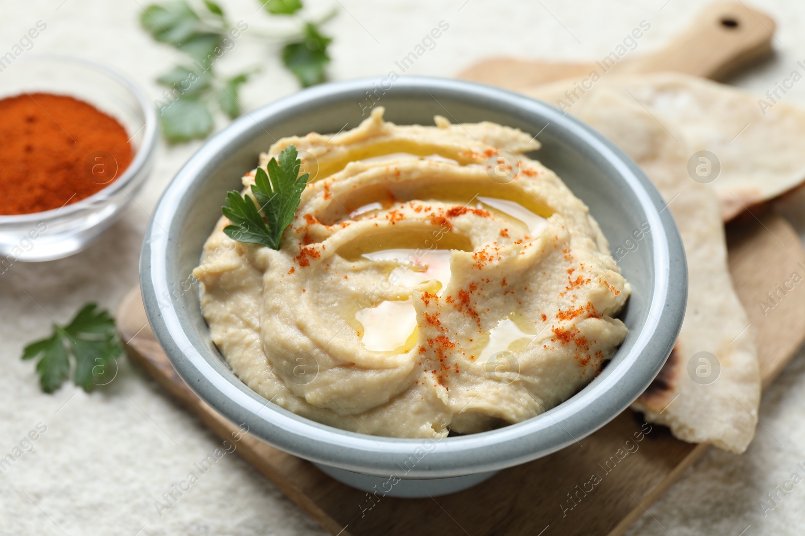 Photo of Delicious hummus with olive oil, parsley and paprika in bowl on white table, closeup