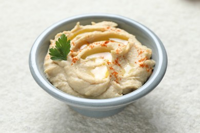 Photo of Delicious hummus with olive oil, parsley and paprika in bowl on white textured table, closeup