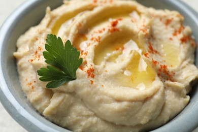 Photo of Delicious hummus with olive oil, parsley and paprika in bowl on white table, closeup