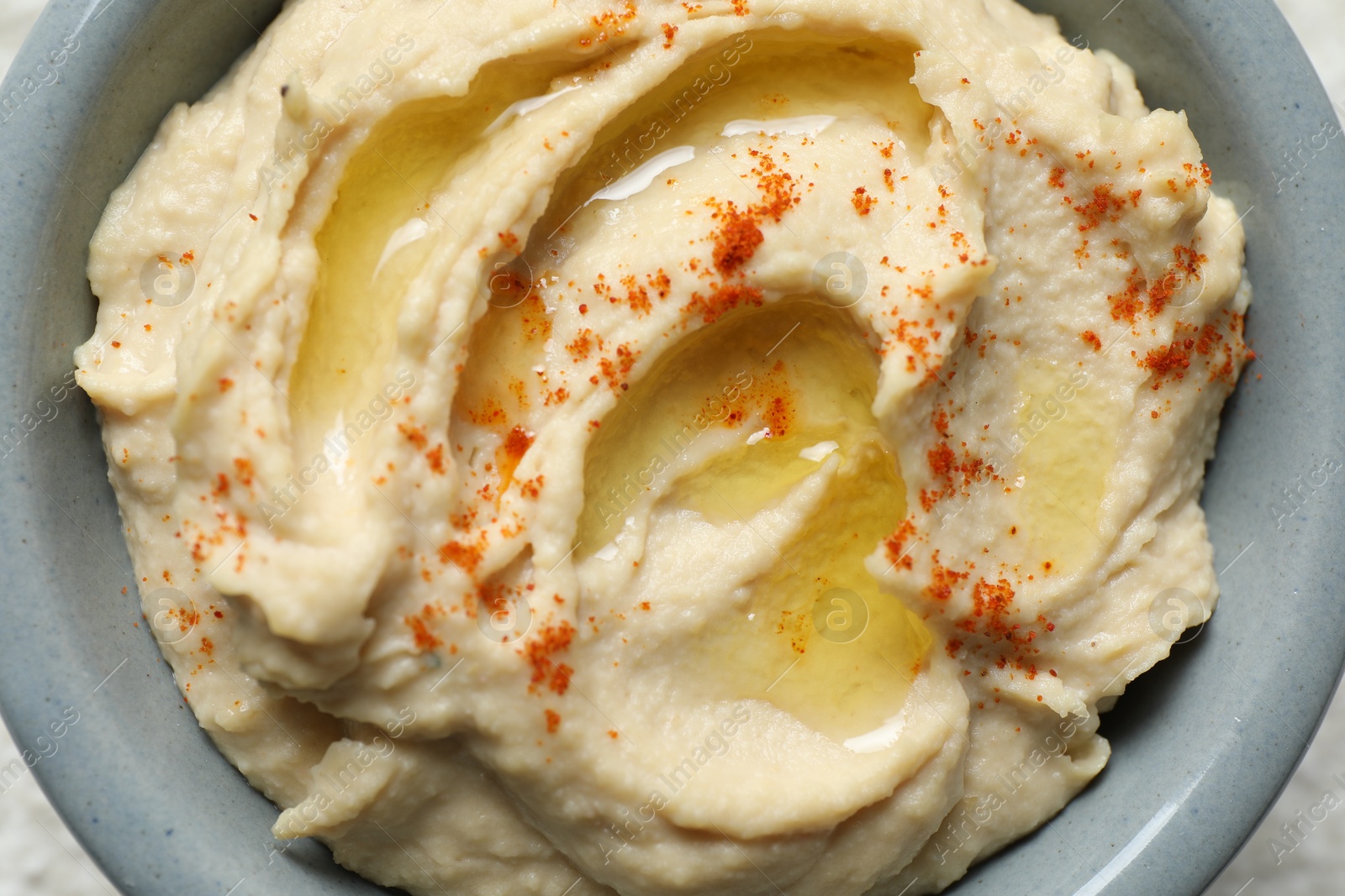 Photo of Delicious hummus with olive oil and paprika in bowl on table, top view