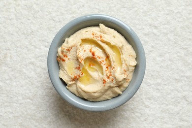 Delicious hummus with olive oil and paprika in bowl on white textured table, top view