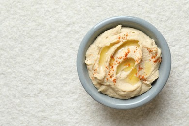 Photo of Delicious hummus with olive oil and paprika in bowl on white textured table, top view. Space for text