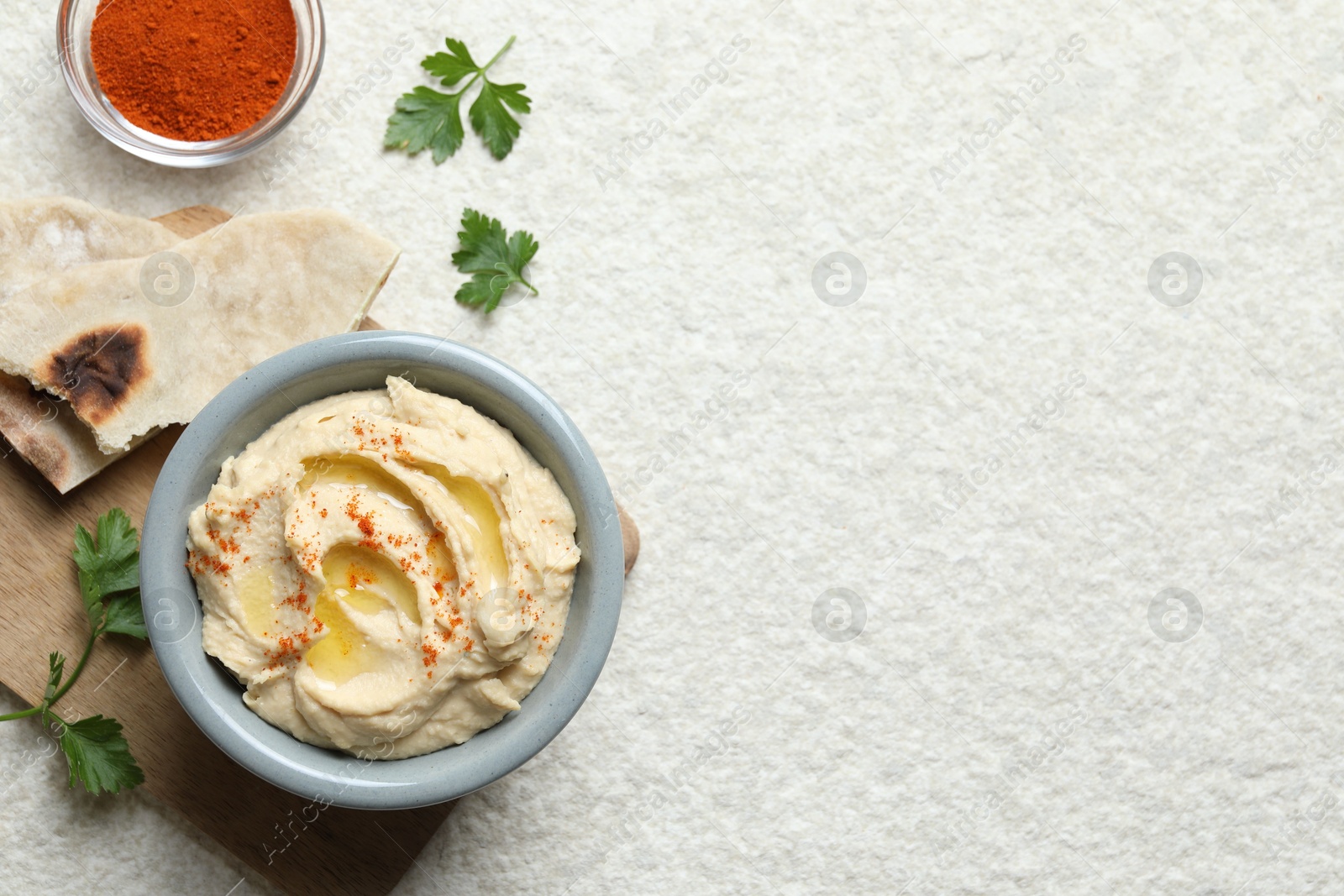 Photo of Delicious hummus with olive oil and paprika served on white textured table, flat lay. Space for text