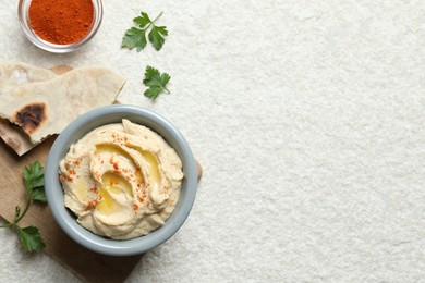 Delicious hummus with olive oil and paprika served on white textured table, flat lay. Space for text