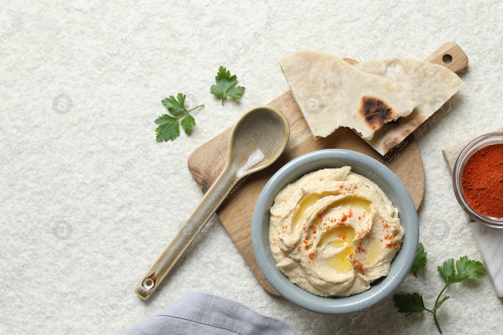 Photo of Delicious hummus with olive oil and paprika served on white textured table, flat lay