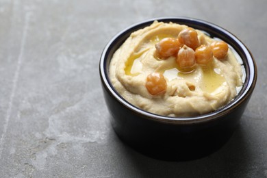 Photo of Delicious hummus with olive oil and chickpeas in bowl on grey textured table