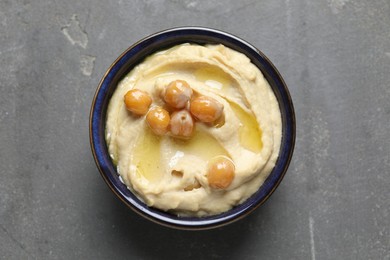 Photo of Delicious hummus with olive oil and chickpeas in bowl on grey textured table, top view