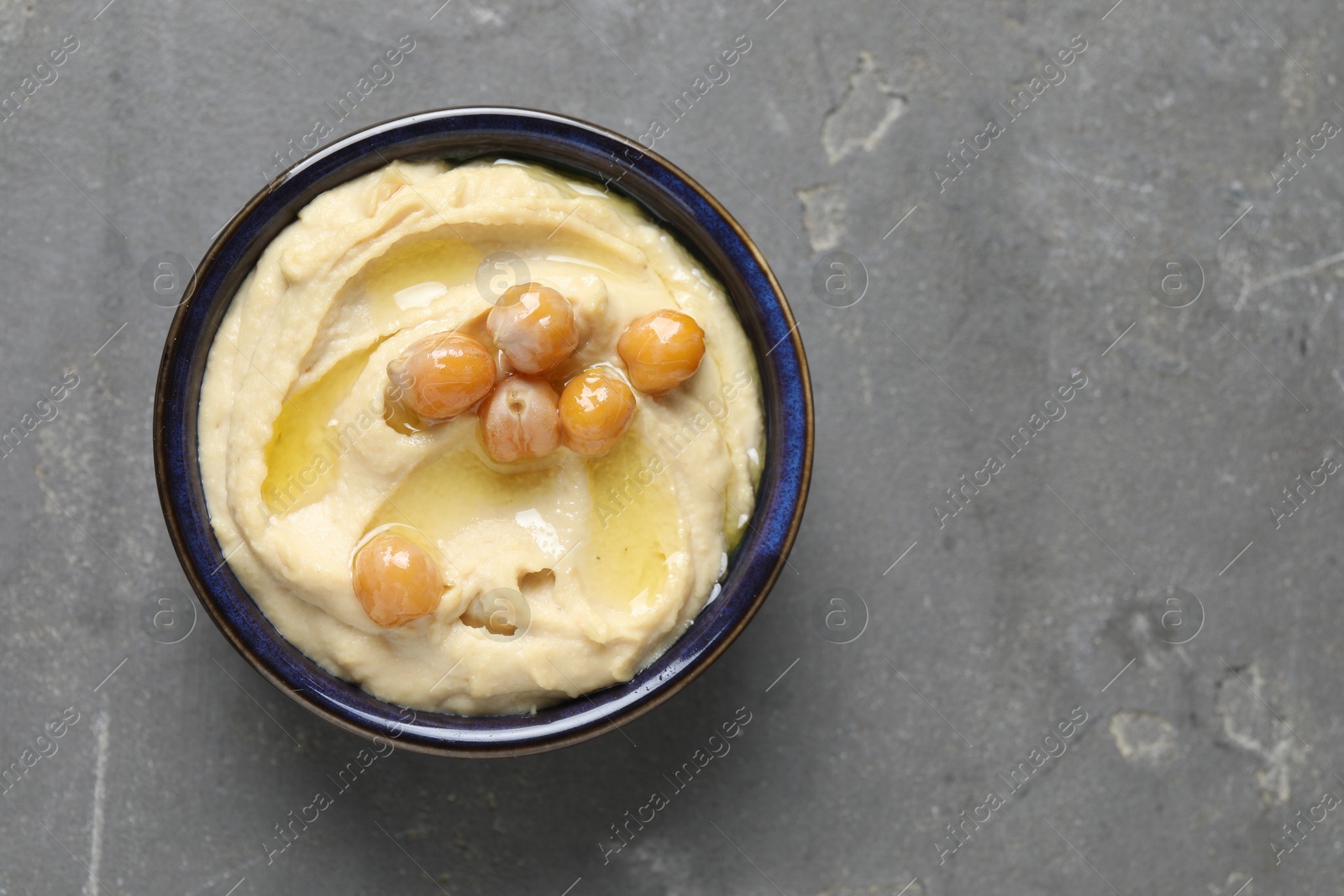 Photo of Delicious hummus with olive oil and chickpeas in bowl on grey textured table, top view. Space for text