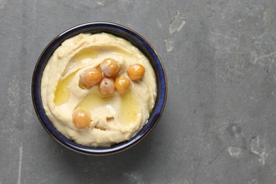 Delicious hummus with olive oil and chickpeas in bowl on grey textured table, top view. Space for text