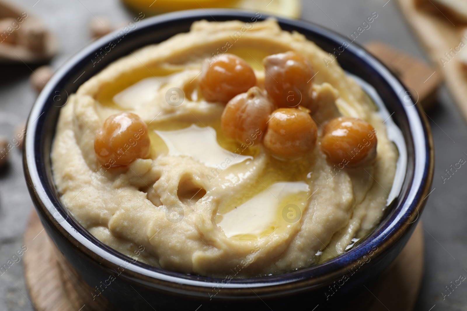 Photo of Delicious hummus with olive oil and chickpeas in bowl on grey table, closeup