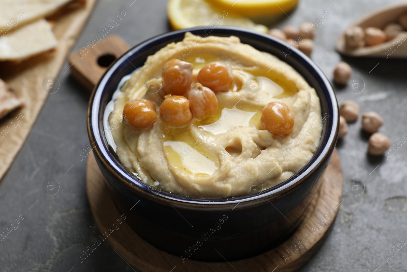 Photo of Delicious hummus with olive oil and chickpeas in bowl on grey table, closeup