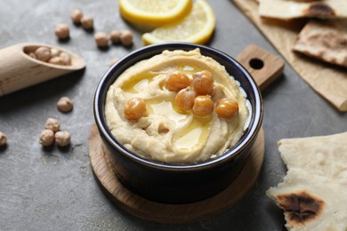 Photo of Delicious hummus with olive oil and chickpeas in bowl on grey table