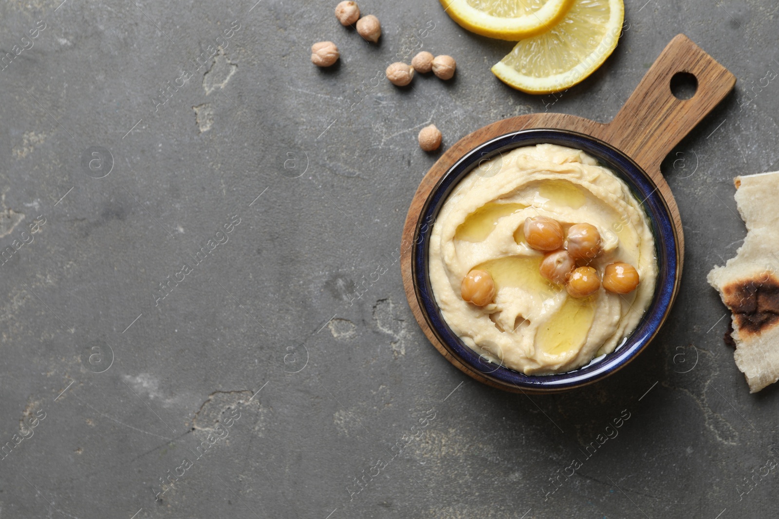 Photo of Delicious hummus with olive oil, chickpeas, lemon and pita on grey textured table, flat lay. Space for text