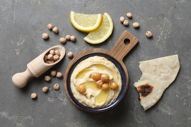 Delicious hummus with olive oil, chickpeas, lemon and pita on grey textured table, flat lay