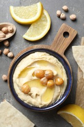 Photo of Delicious hummus with olive oil, chickpeas, lemon and pita on grey textured table, flat lay