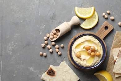 Delicious hummus with olive oil, chickpeas, lemon and pita on grey textured table, flat lay