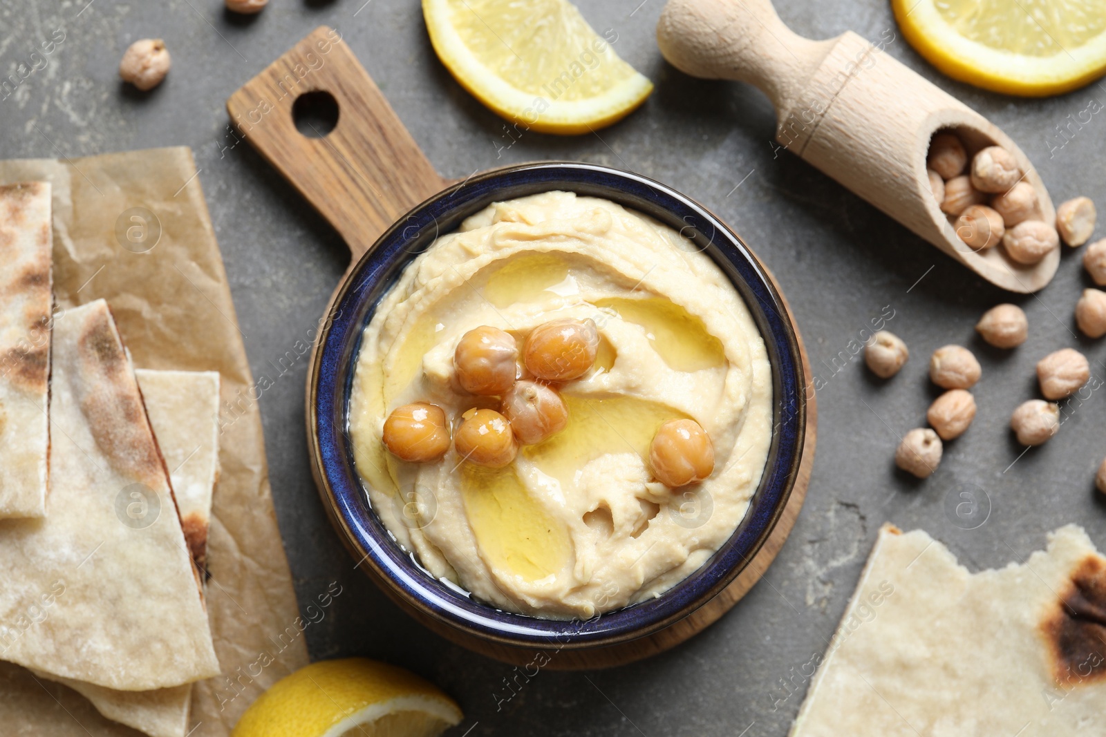 Photo of Delicious hummus with olive oil, chickpeas, lemon and pita on grey textured table, flat lay