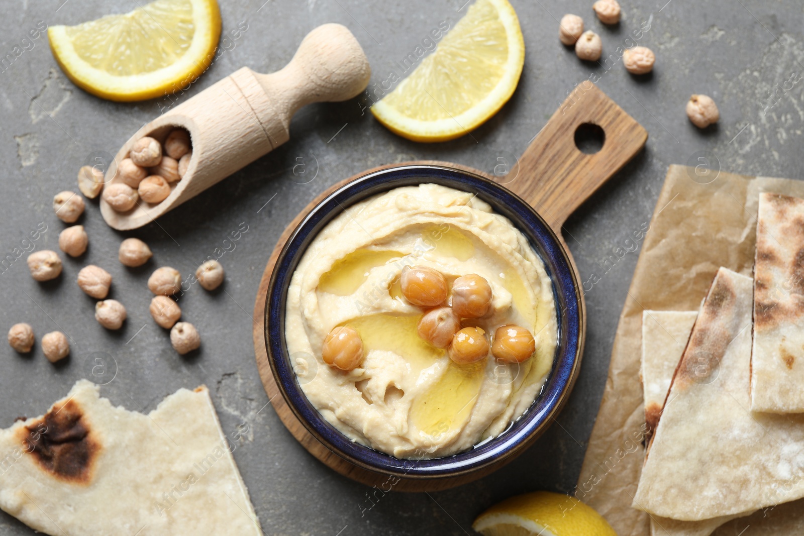 Photo of Delicious hummus with olive oil, chickpeas, lemon and pita on grey textured table, flat lay