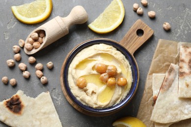 Photo of Delicious hummus with olive oil, chickpeas, lemon and pita on grey textured table, flat lay